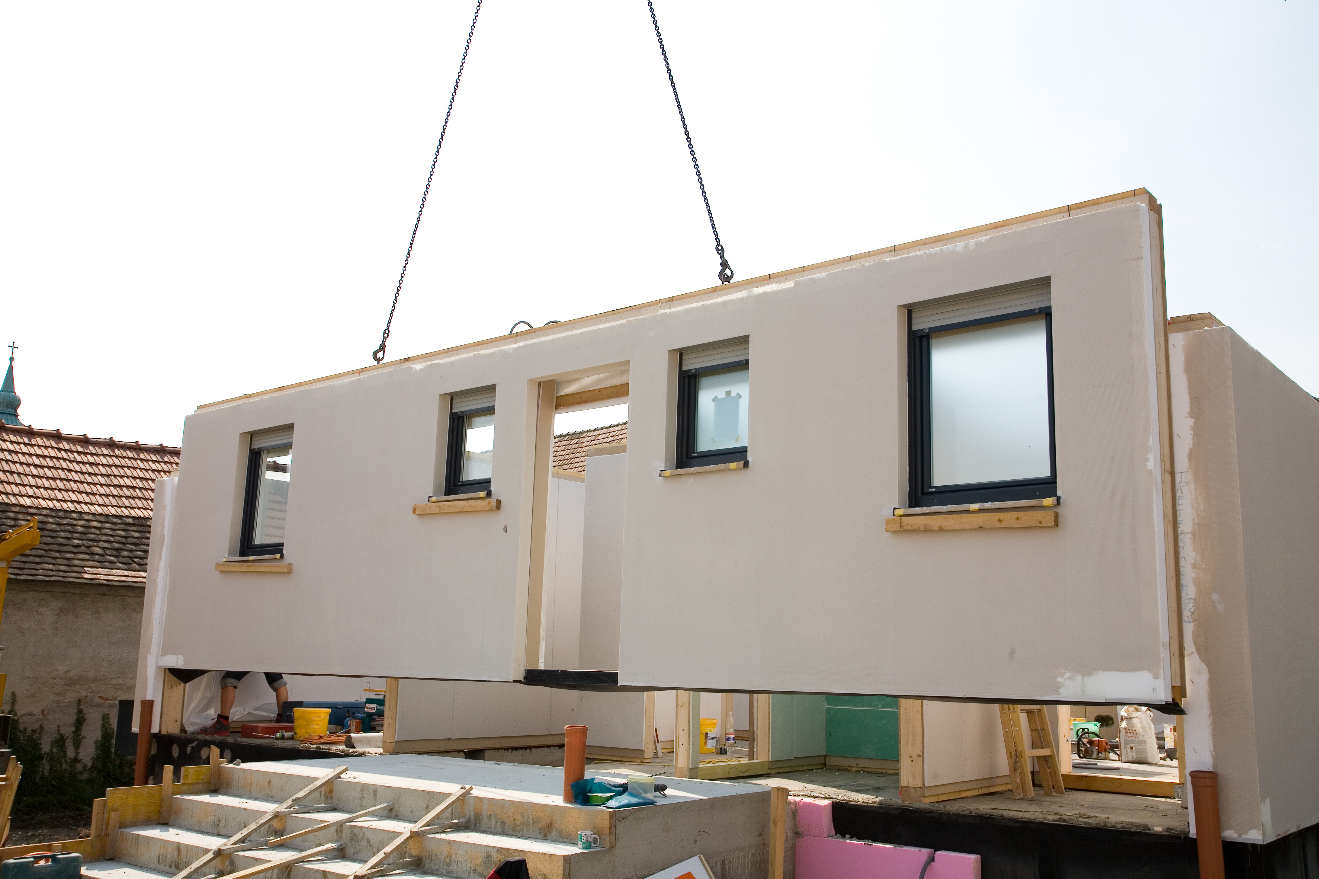 A photo of a crane placing a pre-built wall of a house.